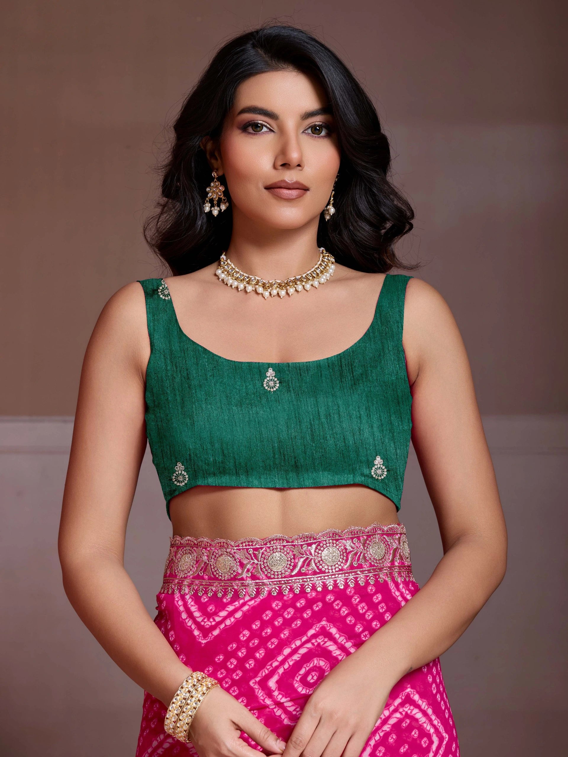Woman wearing a green blouse and pink skirt with jewelry against a brown background