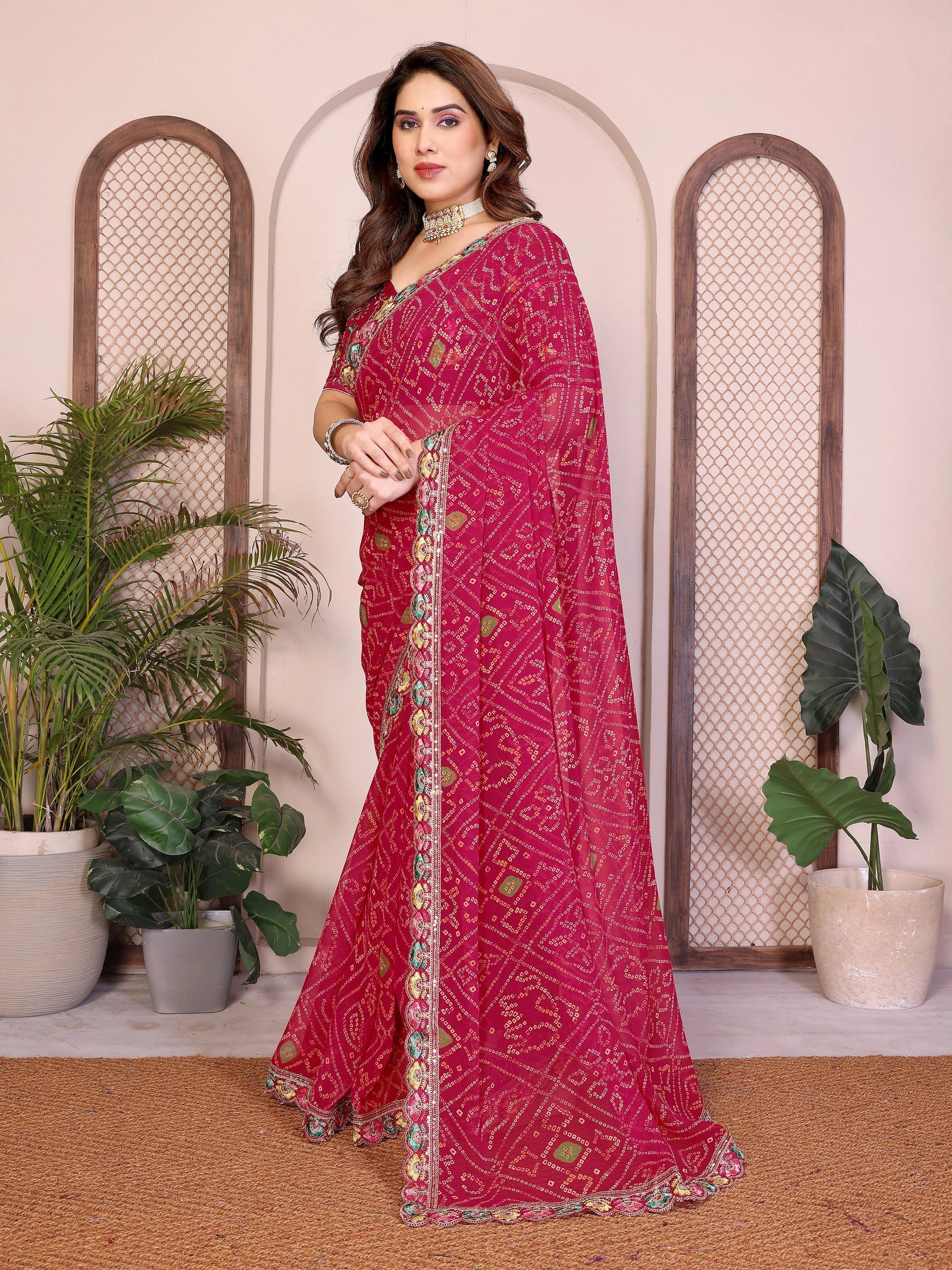 Woman wearing a pink saree with a patterned border in a decorated indoor setting.