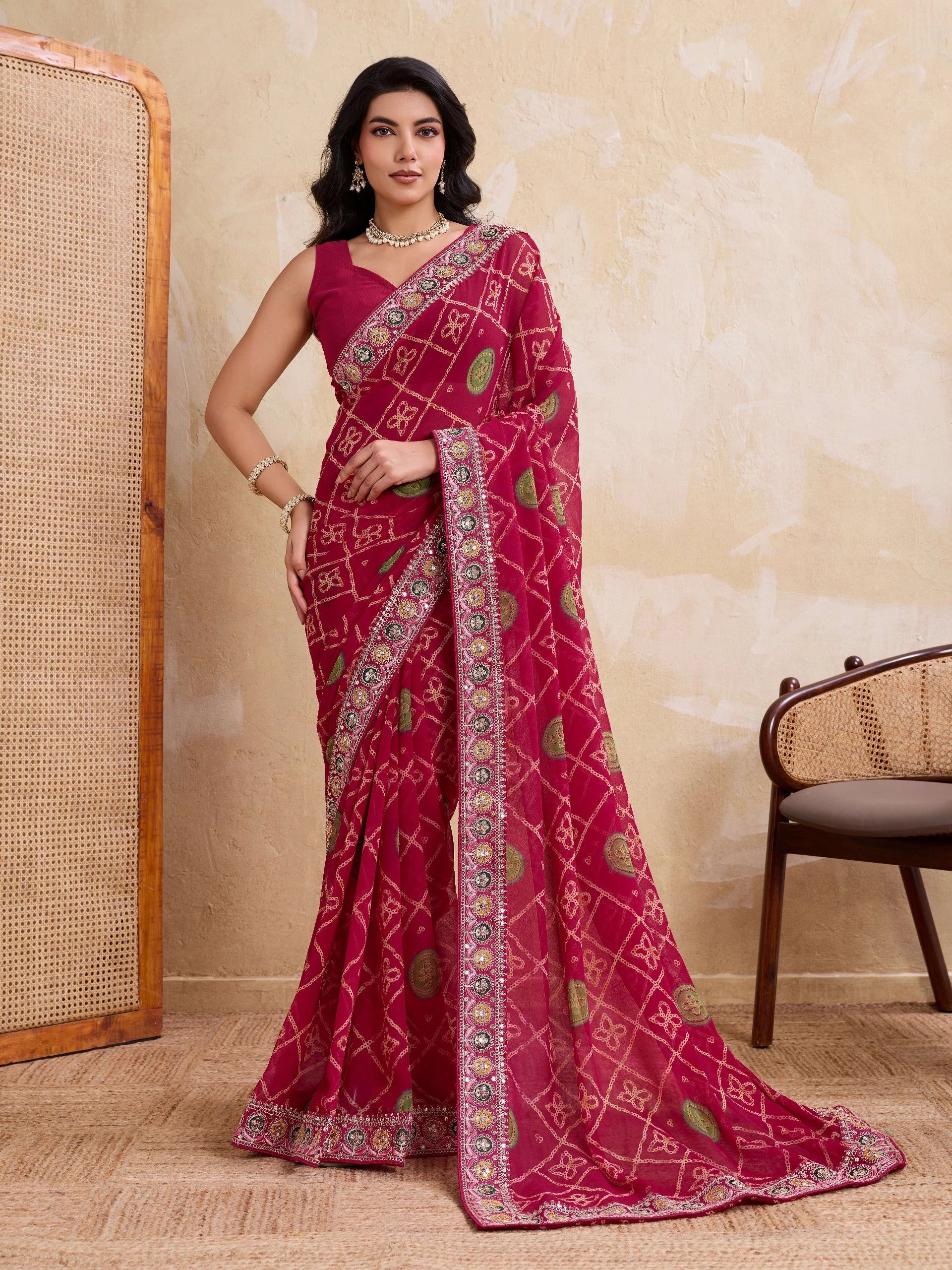 Woman wearing a pink saree with intricate patterns against a beige wall.