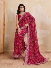 Woman wearing a red saree with intricate patterns against a beige wall.