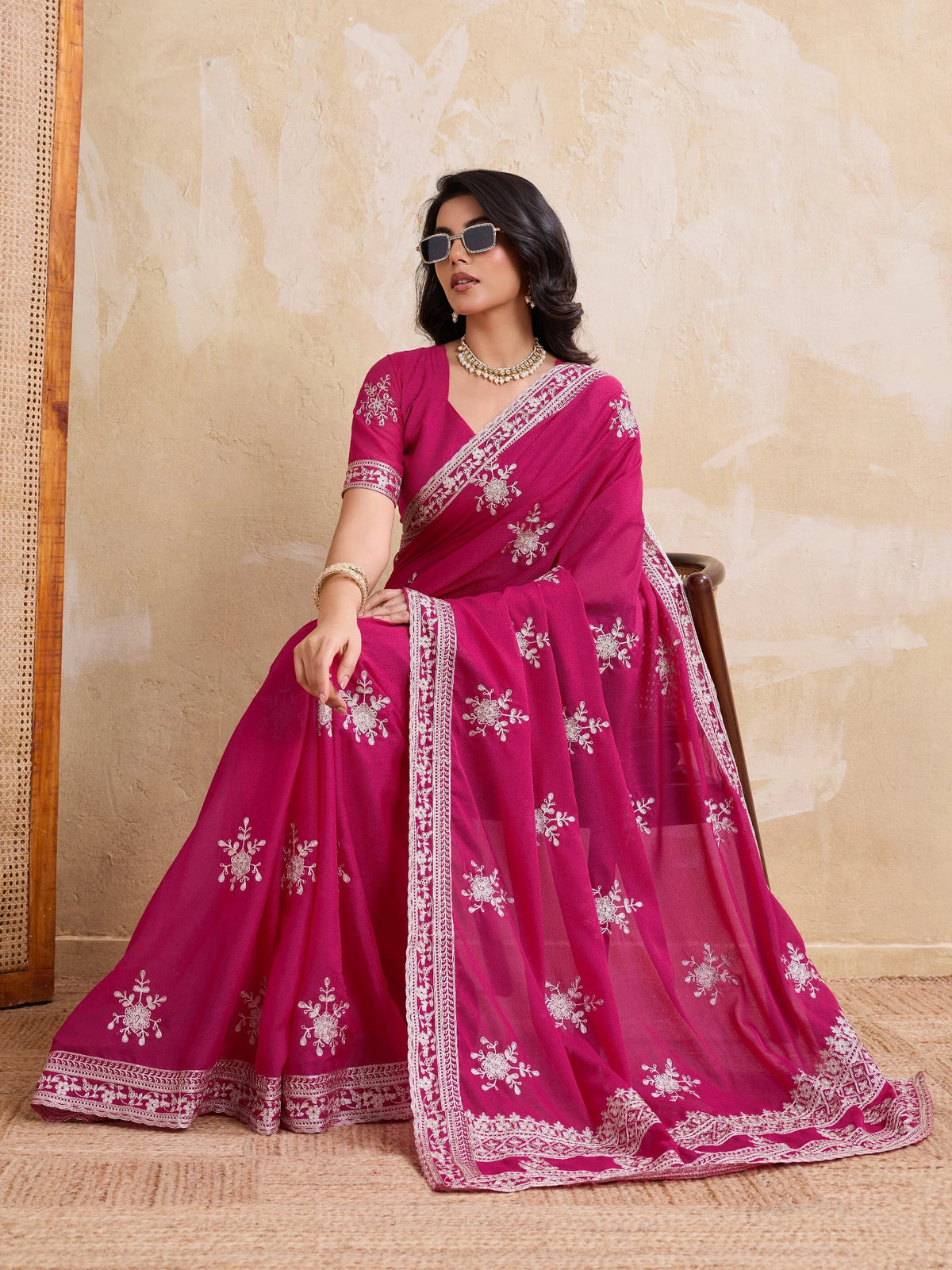 Woman wearing a pink saree with white patterns against a beige wall.