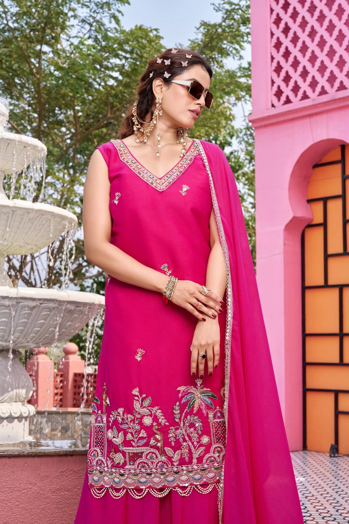 Woman in a pink traditional outfit standing in front of a pink architectural structure.