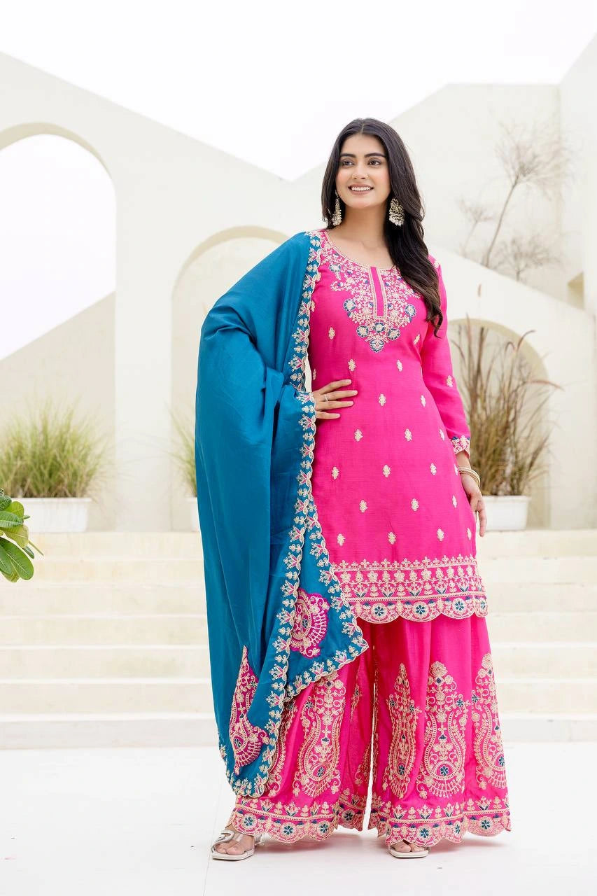 Woman wearing a pink and blue traditional outfit with embroidery in an elegant setting.