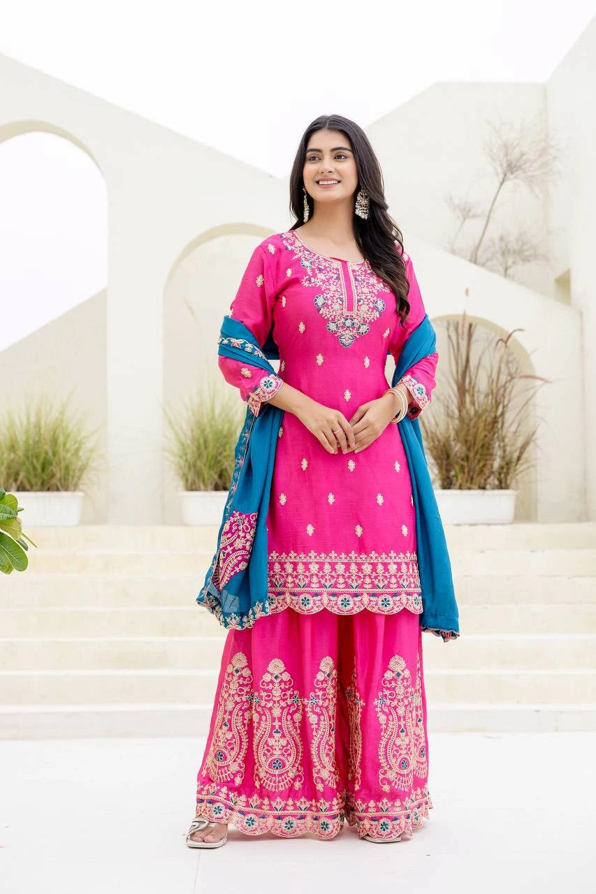 Woman wearing a pink traditional outfit with blue dupatta against a white architectural background