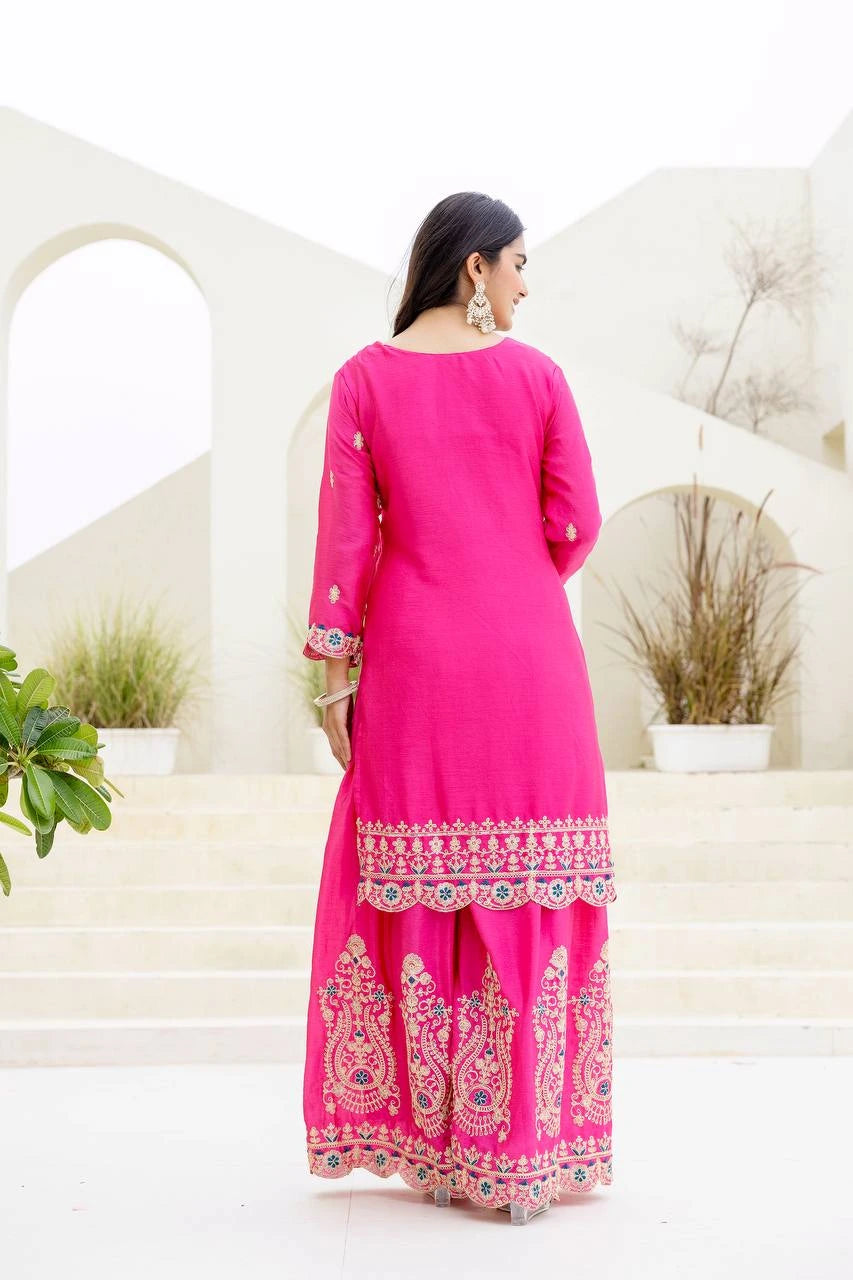 Woman wearing a bright pink traditional outfit with white patterns in an outdoor setting.
