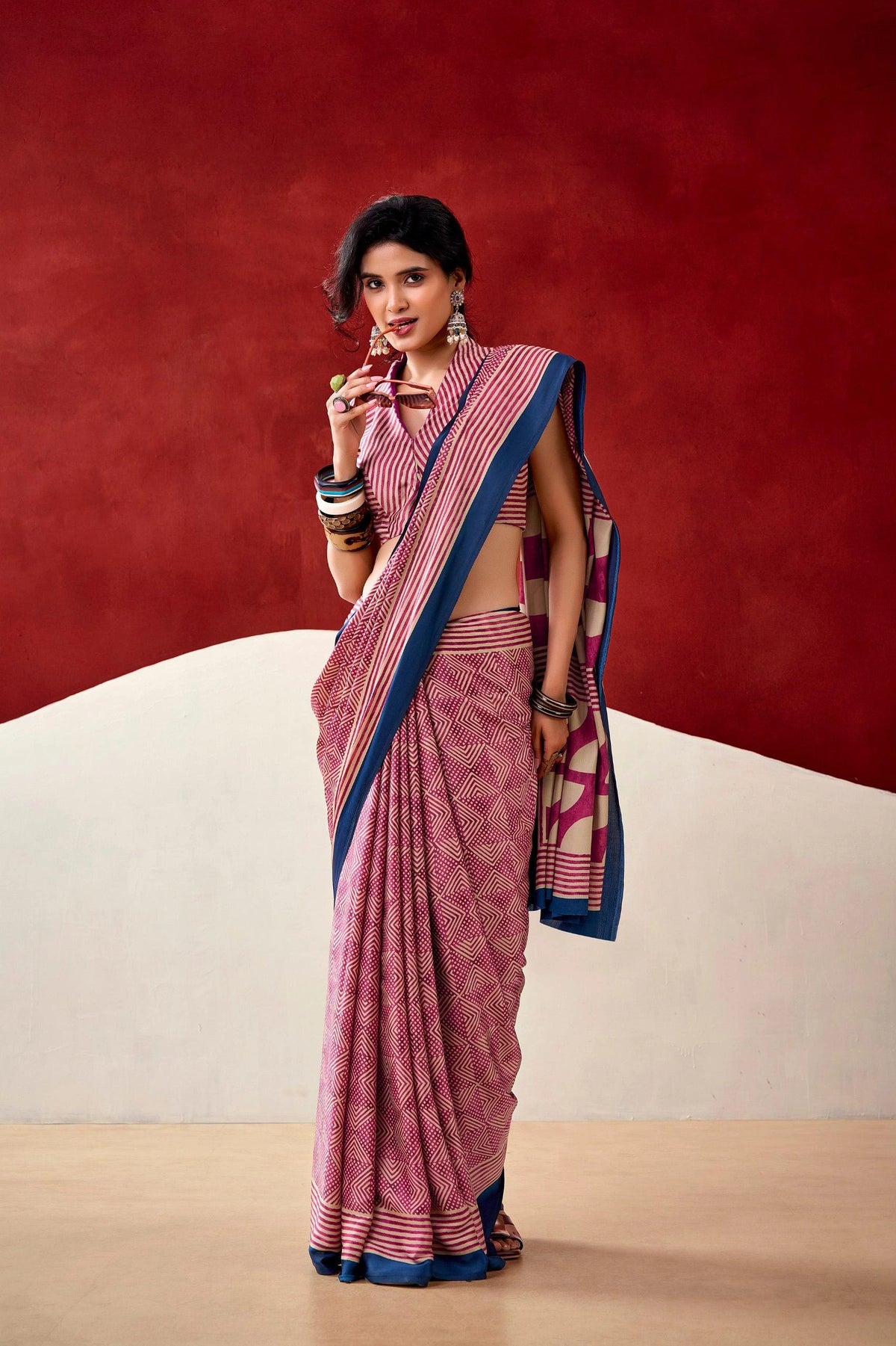 Woman wearing a pink saree with blue border against a red and beige background