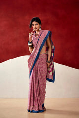 Woman wearing a pink saree with blue border against a red and beige background