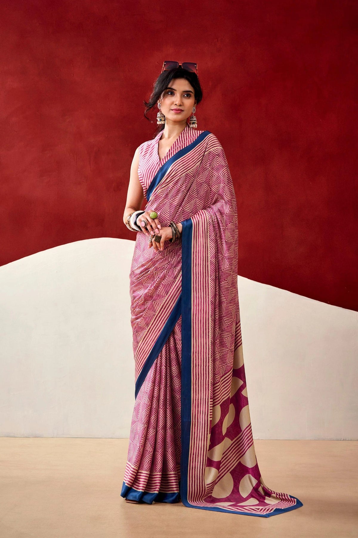 Woman wearing a pink saree with a blue border against a red and beige background