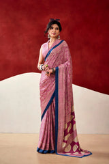 Woman wearing a pink saree with a blue border against a red and beige background