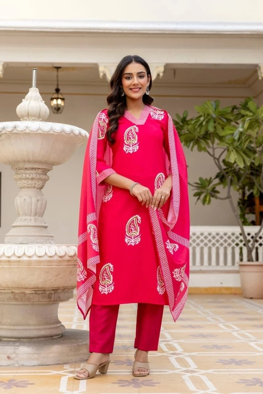 Woman in a bright pink traditional outfit standing in an outdoor setting with decorative elements.