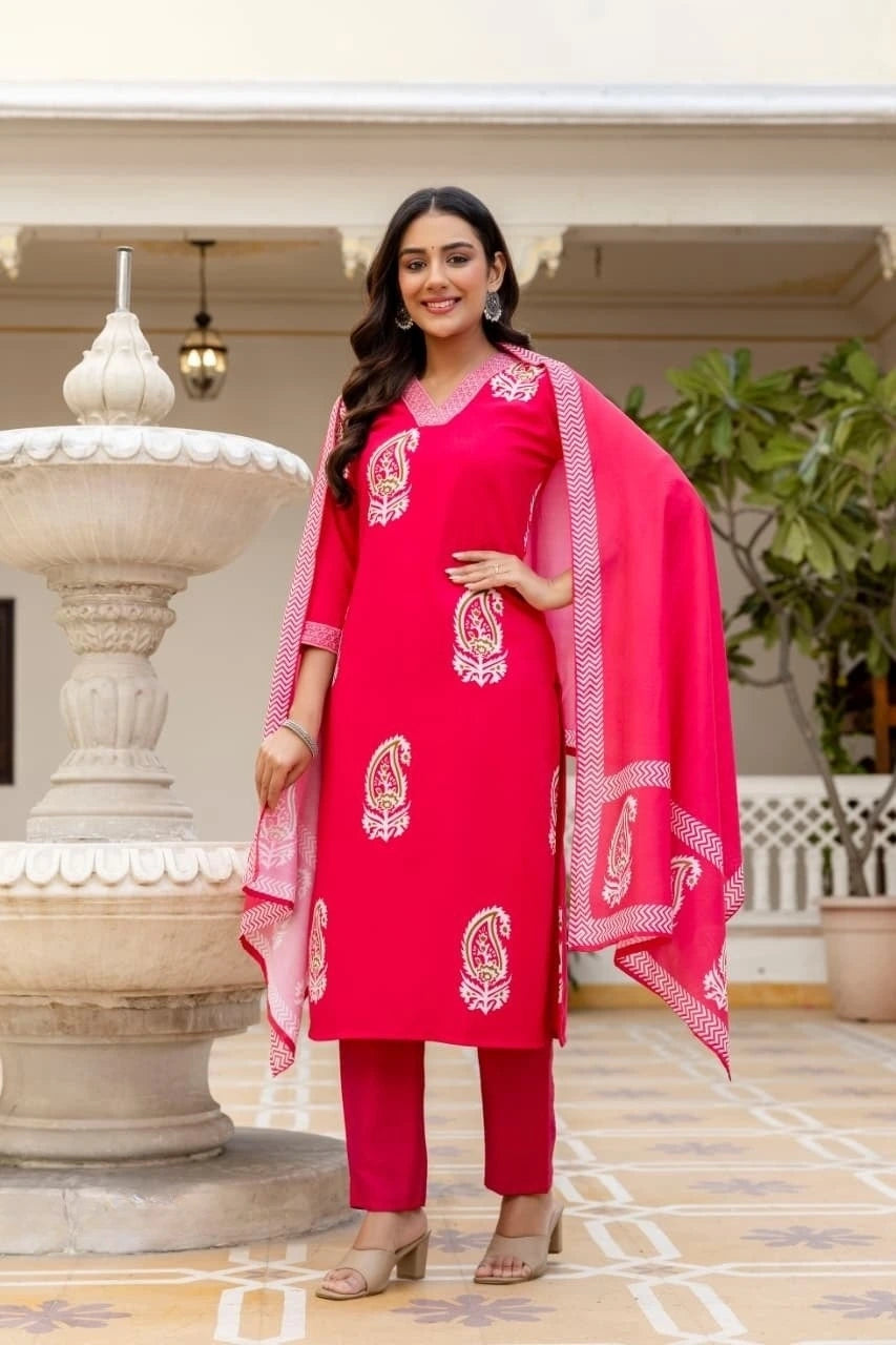Woman in a pink traditional outfit standing outdoors with decorative elements in the background