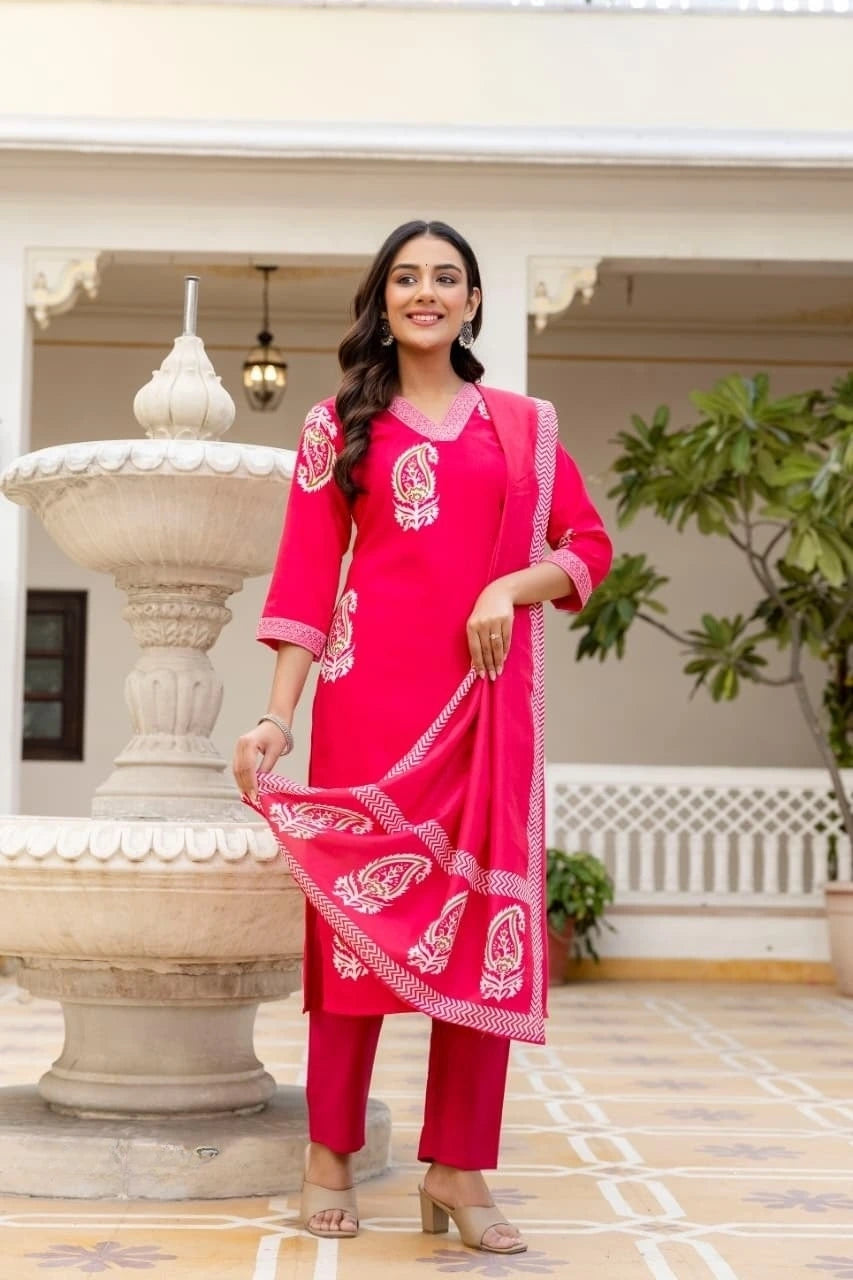 Woman in a bright pink traditional outfit with white patterns standing in an outdoor setting.