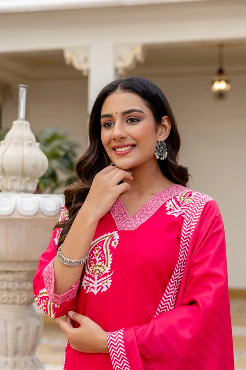 Woman wearing a bright pink traditional outfit with white embroidery in an outdoor setting.