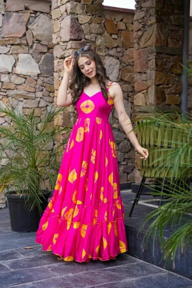 Woman in a pink dress with yellow patterns standing outdoors against a stone wall.