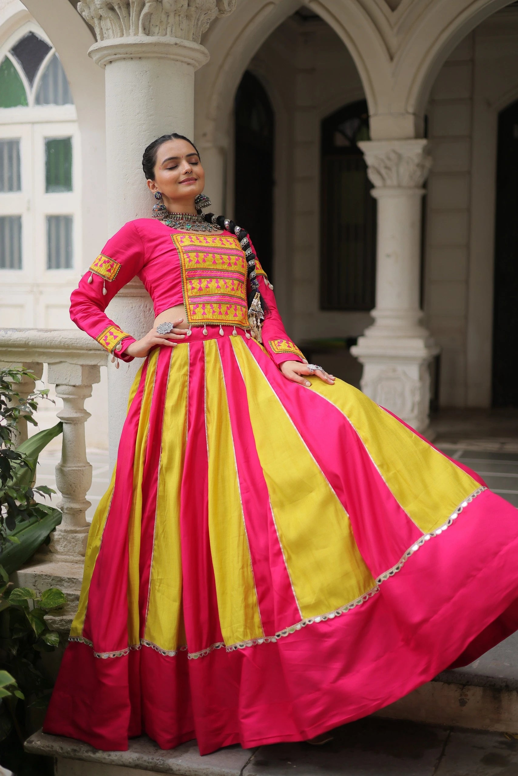 Woman in a vibrant pink and yellow traditional outfit standing in an architectural setting.