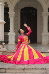 Person in a vibrant pink and yellow traditional outfit standing in front of an archway.