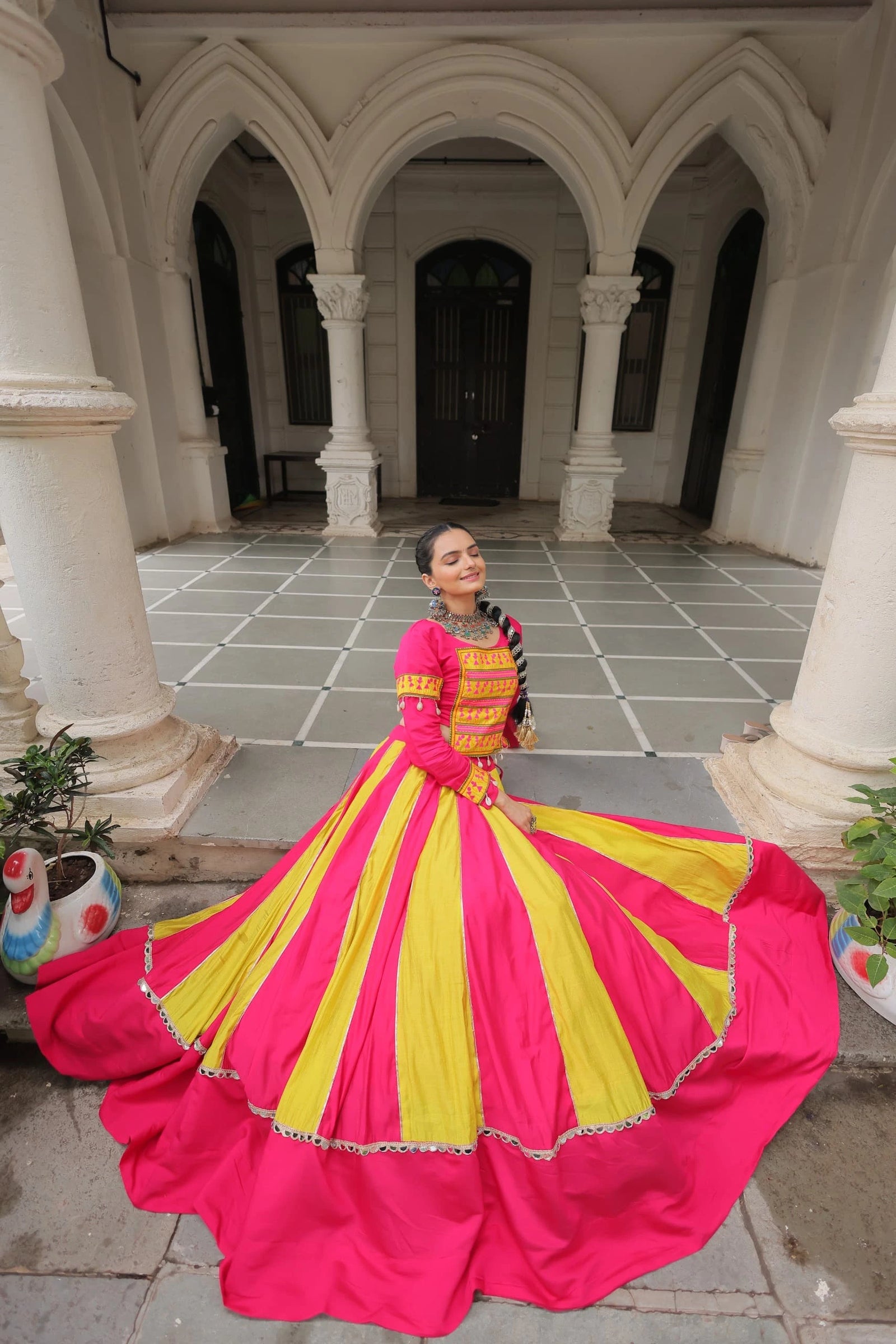 Woman in a pink and yellow dress standing in an architectural courtyard.