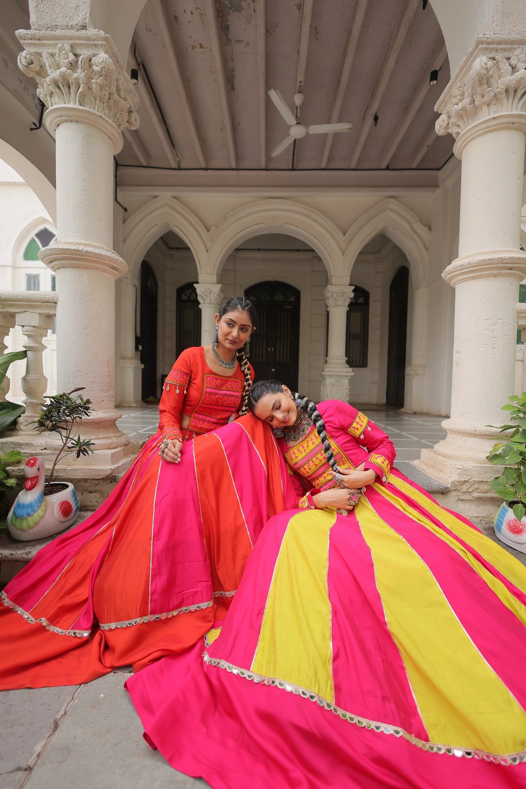 Two women in colorful traditional dresses sitting in a decorative indoor setting.