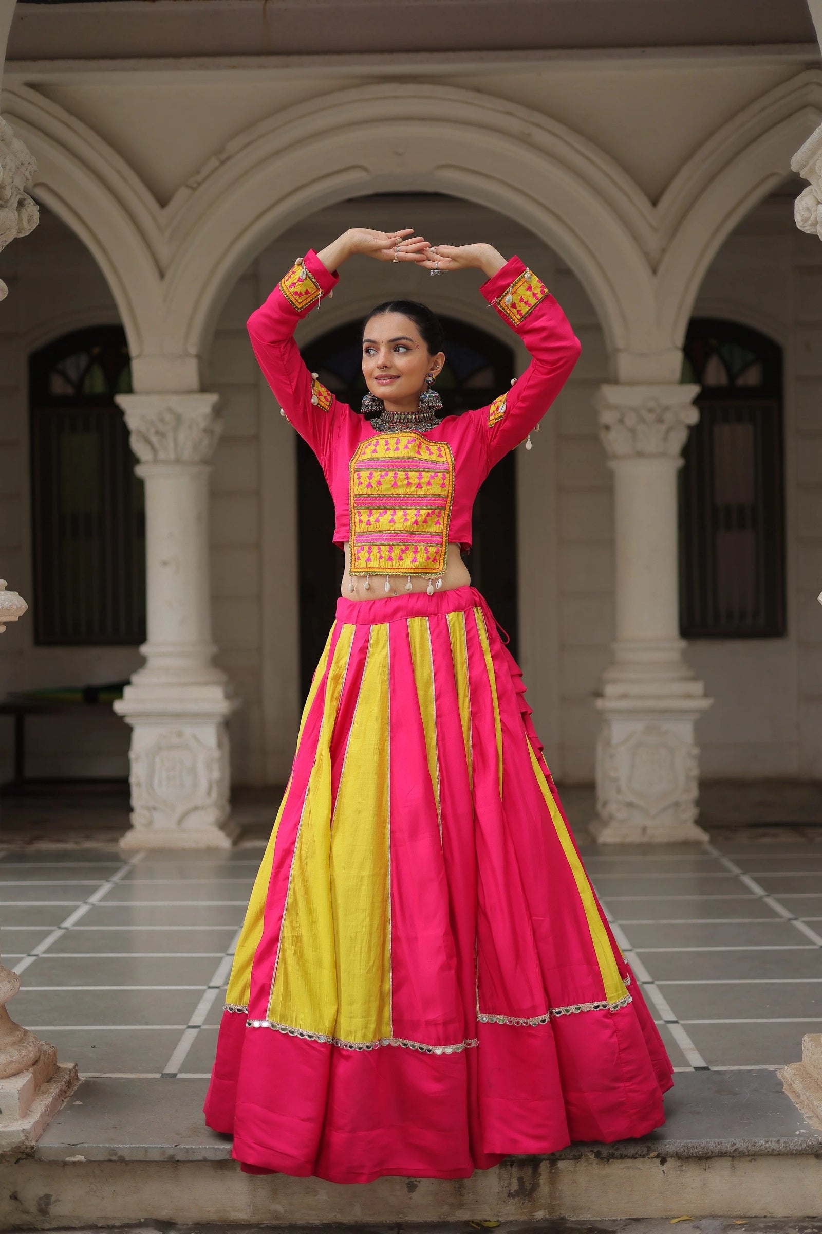 Woman in a vibrant pink and yellow traditional outfit standing in front of architectural columns.