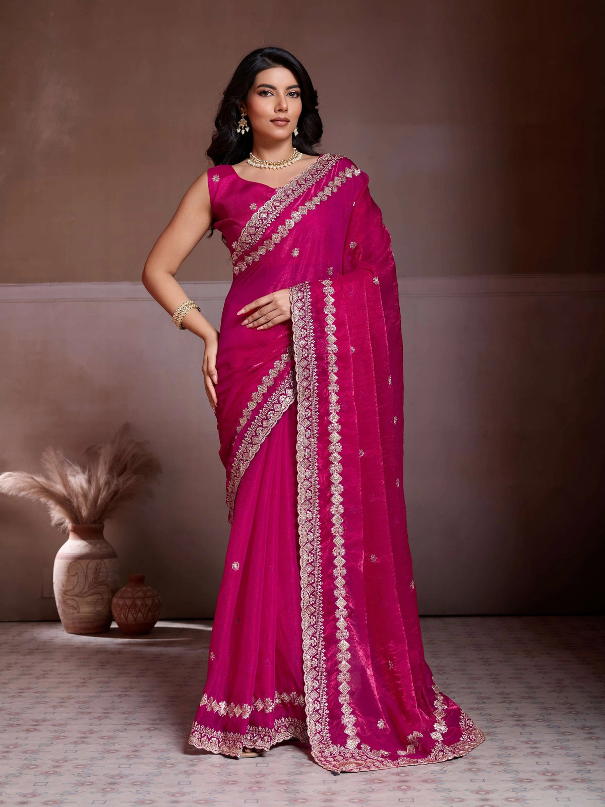 Woman wearing a pink saree with intricate designs against a neutral background