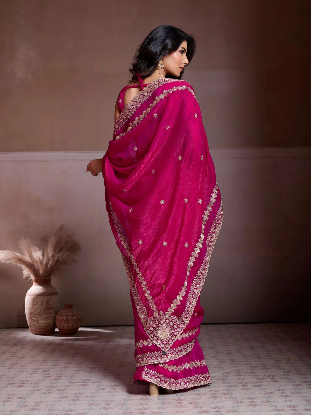 Woman wearing a bright pink saree with gold embroidery against a neutral background
