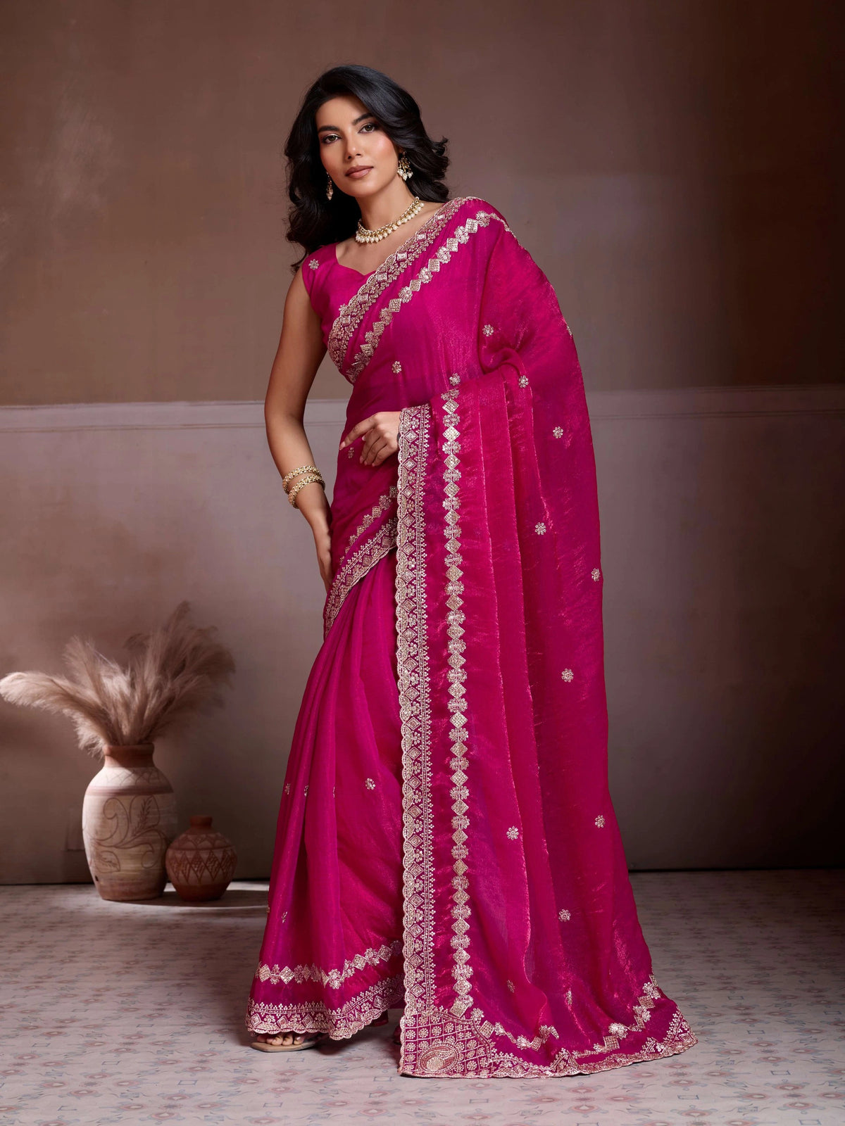 Woman wearing a pink saree with white patterns against a neutral background