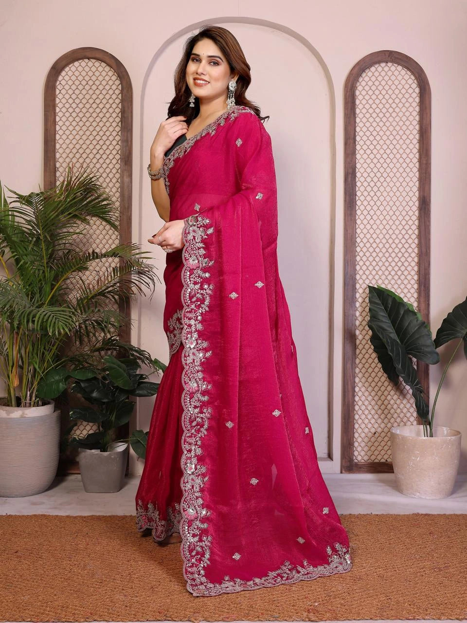 Woman wearing a pink saree with silver embroidery in a decorative setting with plants.