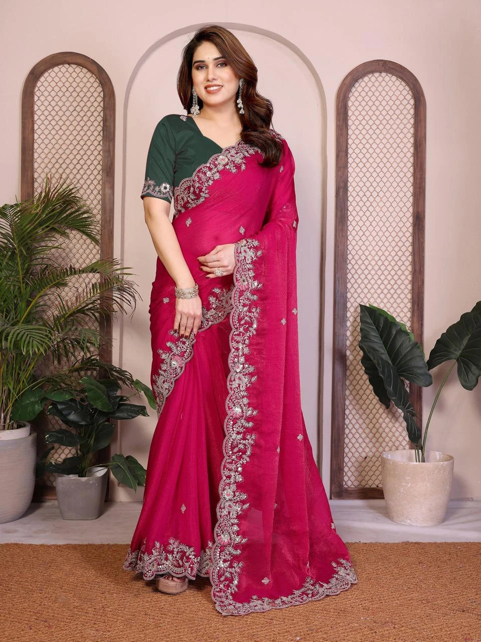 Woman wearing a pink saree with green blouse in an indoor setting with plants.