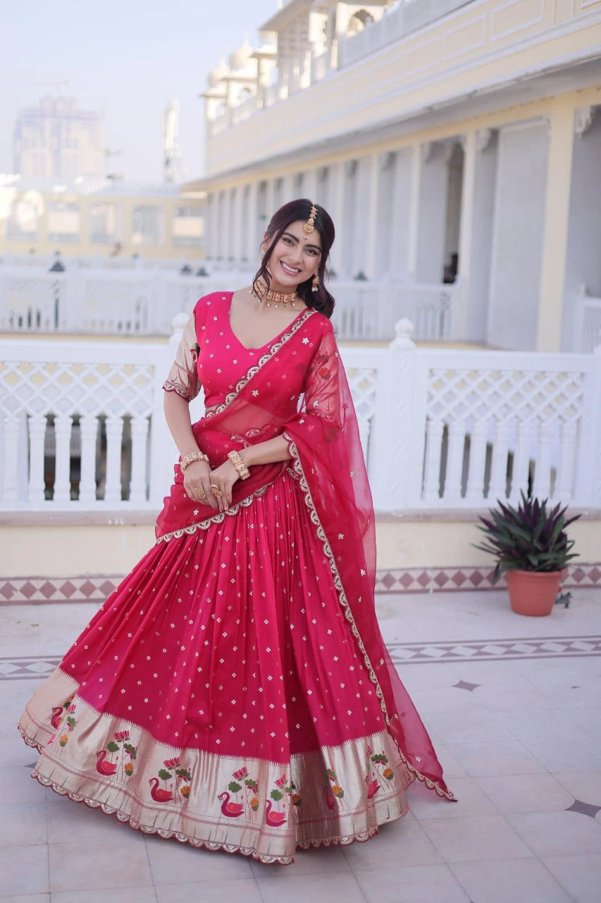Woman in a pink traditional outfit standing on a patio with white columns and a plant in the background.