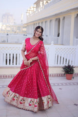 Woman in a pink traditional outfit standing on a patio with white columns and a plant in the background.