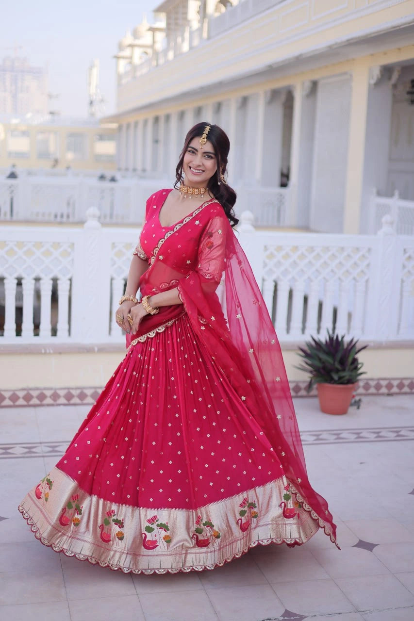 Woman in a red saree with a white building and potted plant in the background