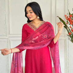 Woman wearing a red traditional outfit with a pink dupatta against a white paneled wall.