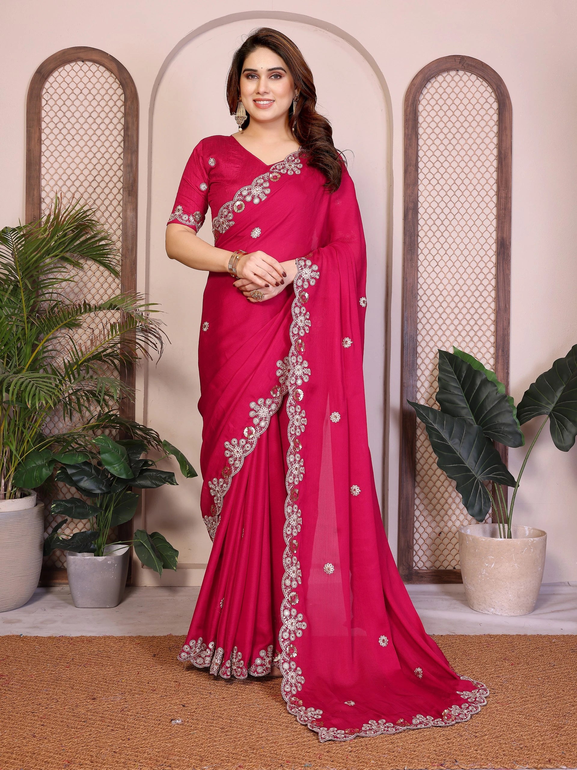 Woman wearing a pink saree with silver embroidery in a decorative setting with plants.