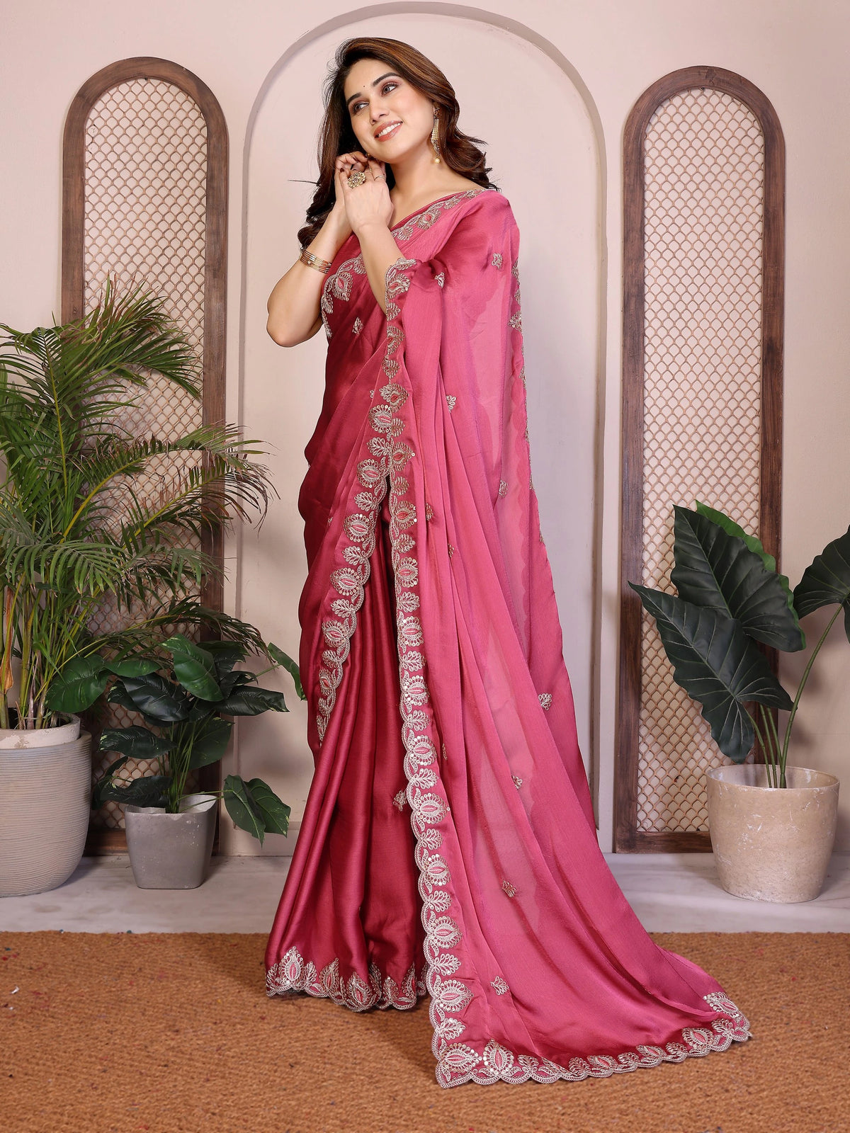 Woman wearing a pink saree with white embroidery in an indoor setting with plants.