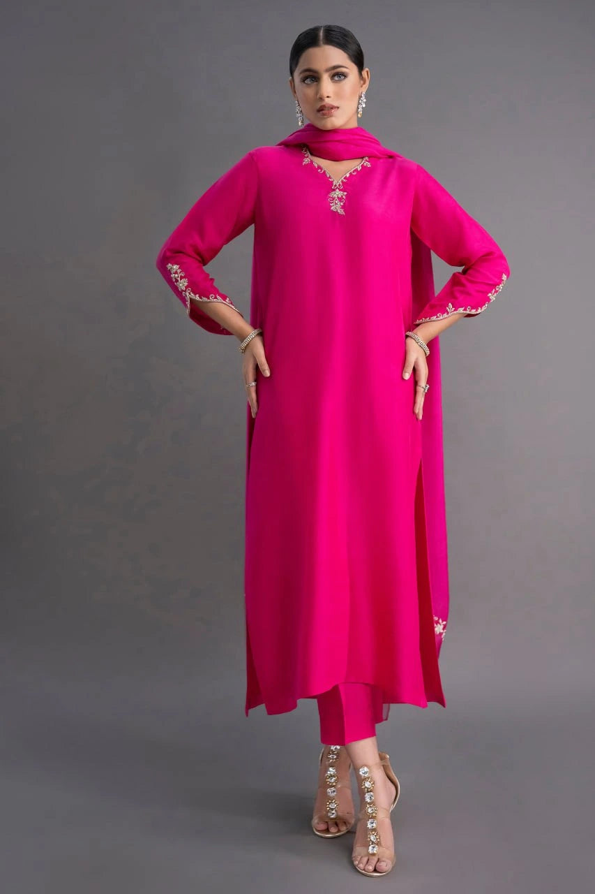 Woman wearing a bright pink traditional outfit with intricate detailing on a gray background