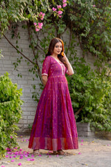 Woman in a pink dress standing outdoors with greenery and flowers around.