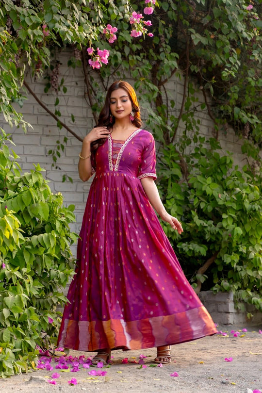 Woman in a magenta dress standing outdoors with greenery and flowers around.