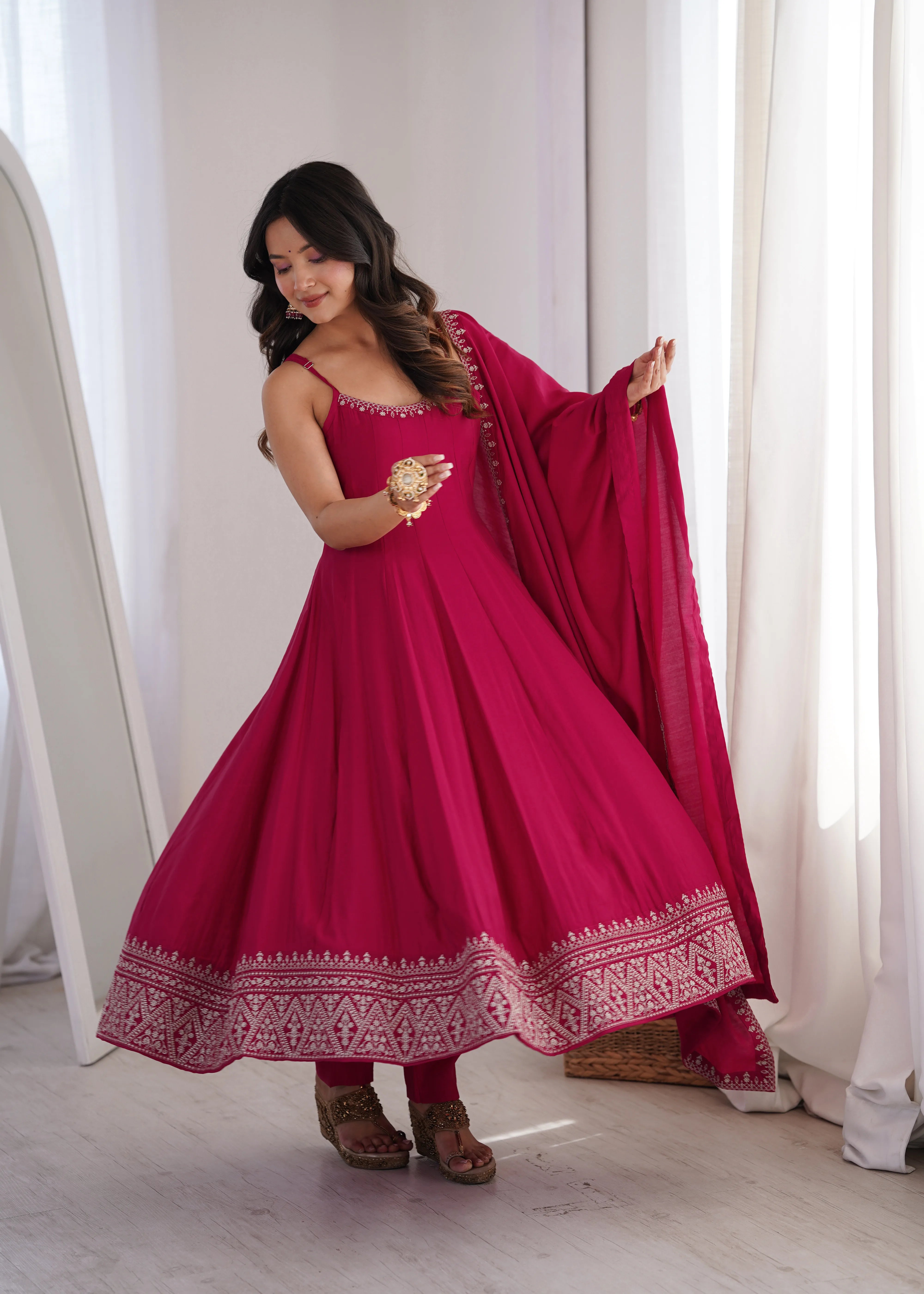 Woman in a red traditional outfit with gold details standing in a bright room.