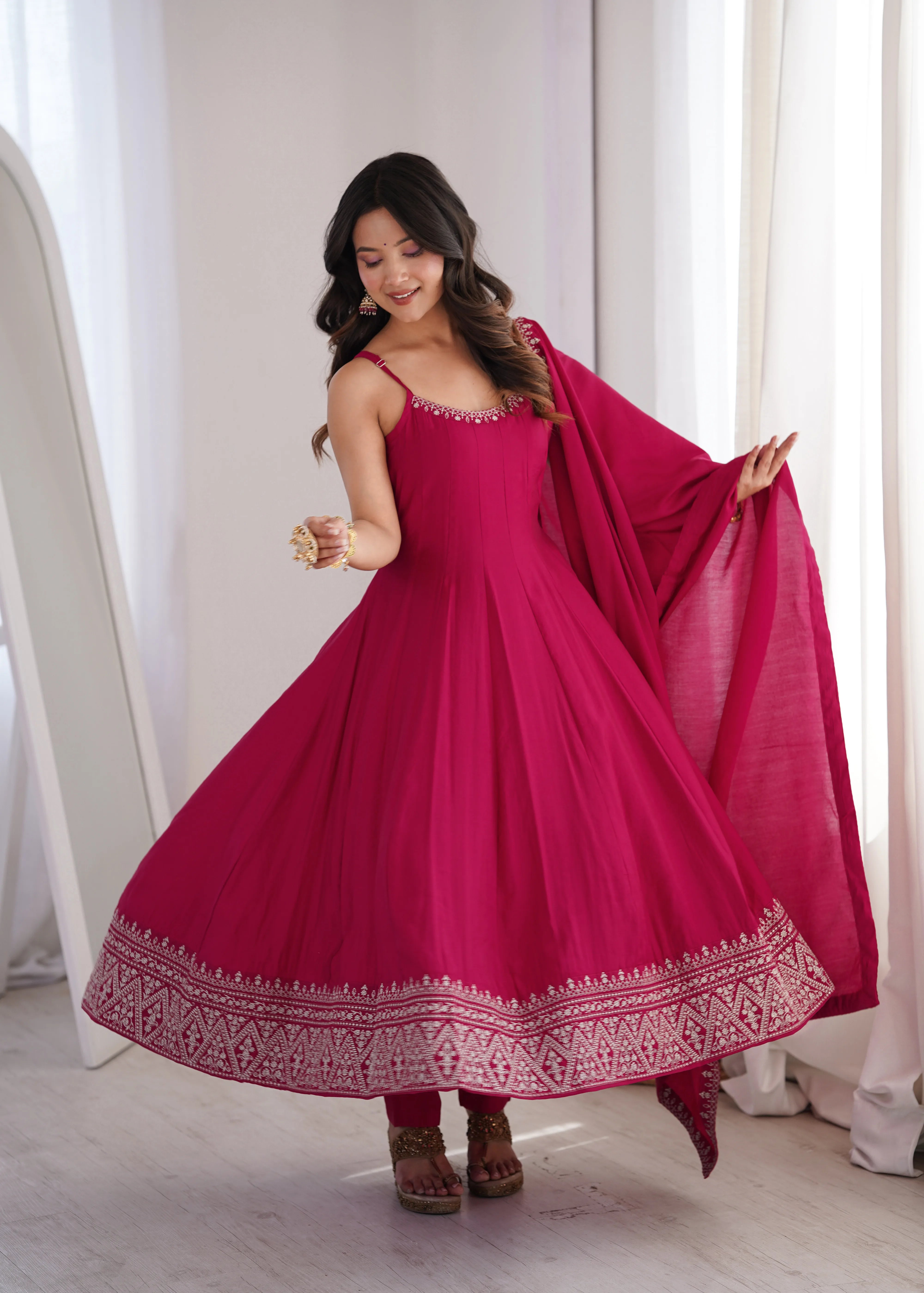 Woman wearing a pink traditional outfit with a matching dupatta in a bright room.