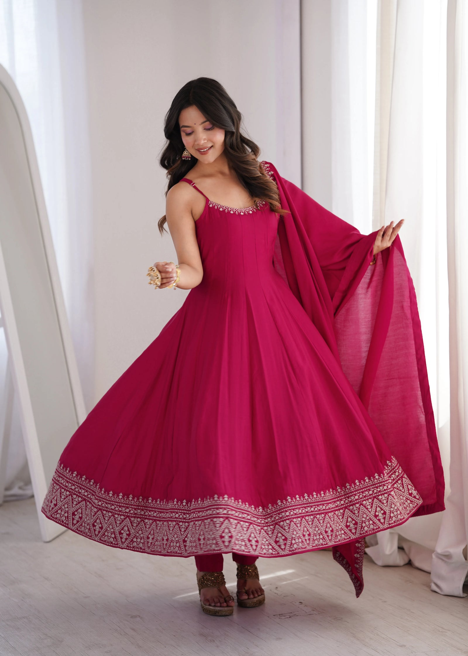 Woman wearing a pink traditional outfit with a matching dupatta in a bright room.