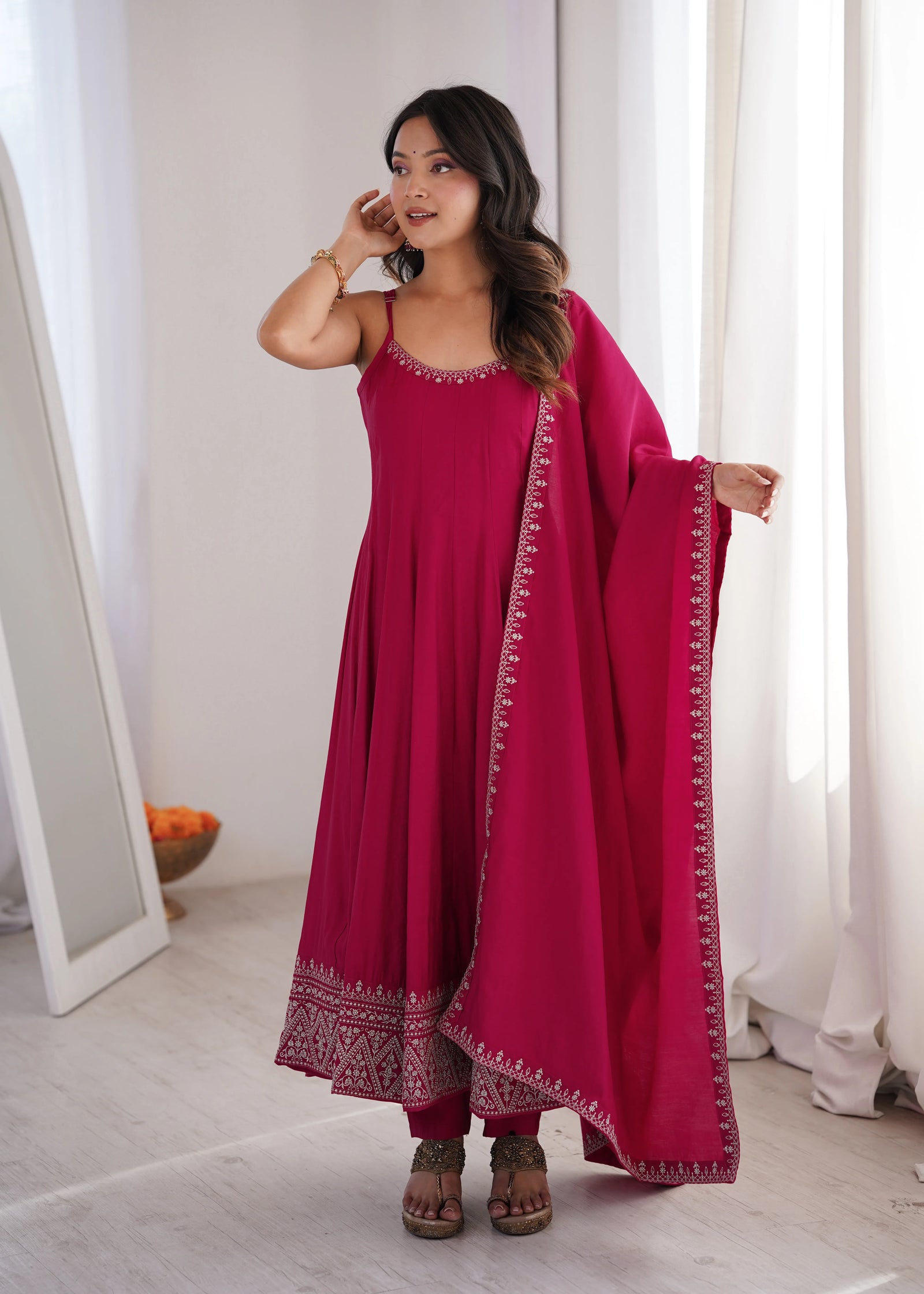 Woman in a pink traditional outfit standing in a room with white walls and a mirror.