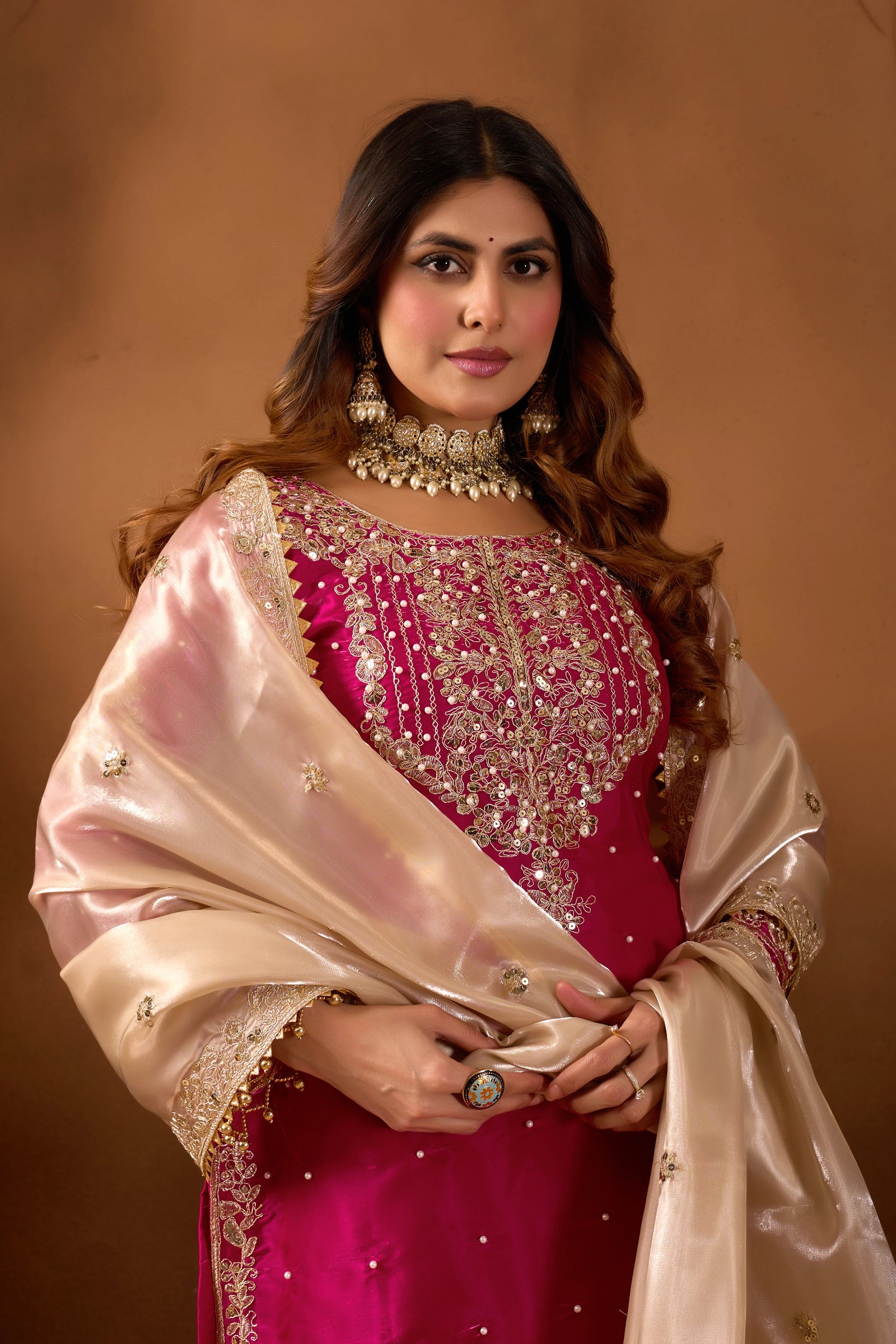 Woman in traditional pink and beige outfit with jewelry against a brown background