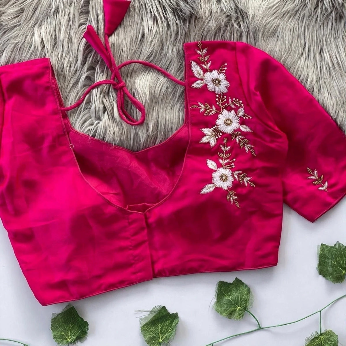 Pink blouse with floral embroidery on a textured surface with green leaves.