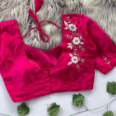 Pink blouse with floral embroidery on a textured surface with green leaves.