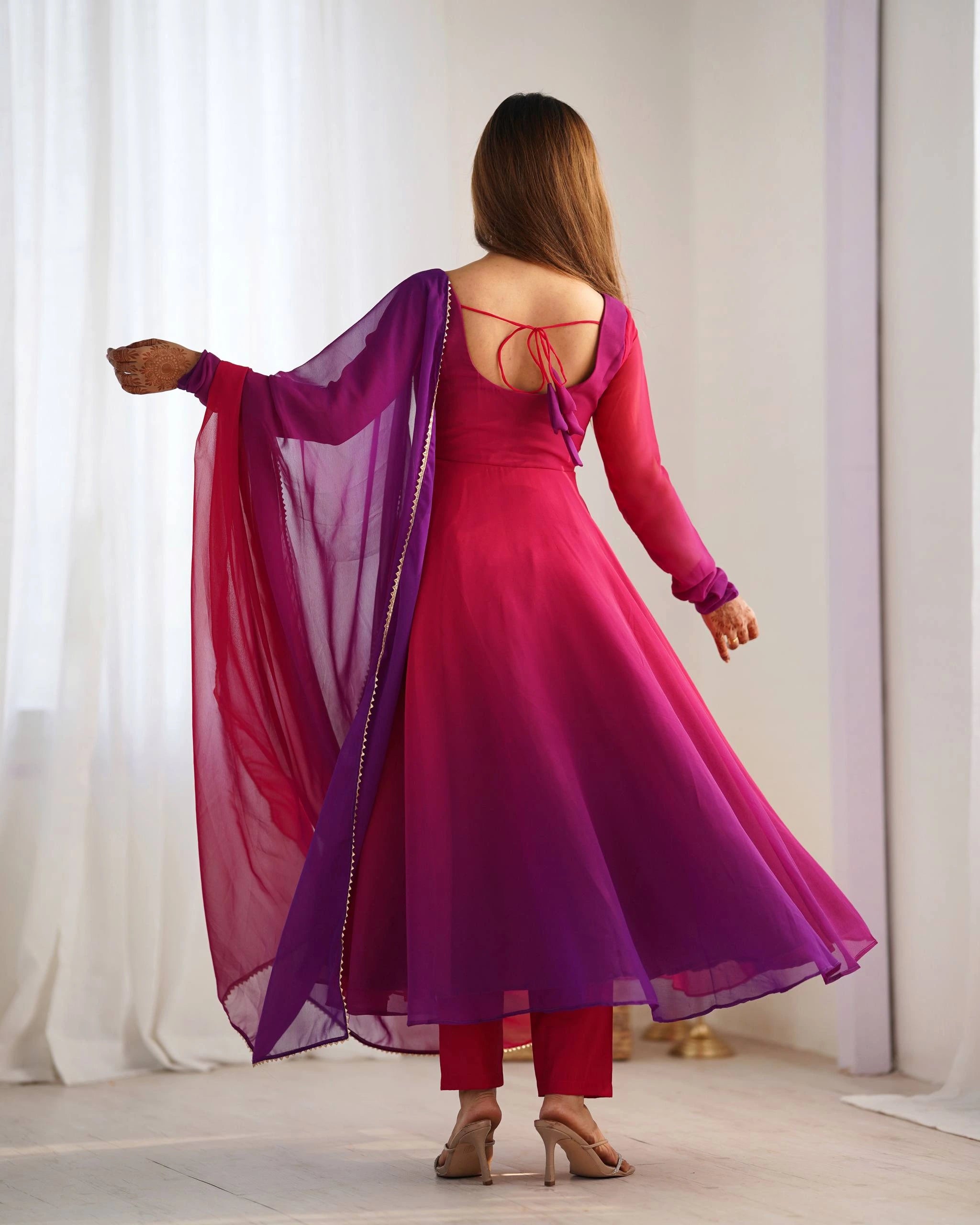 A rear view of a woman modeling a matching magenta and purple Anarkali-style dress, showing the tie-up back detail and deep neckline.