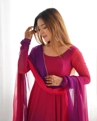 A medium shot of a woman in a magenta and purple Anarkali-style suit with a matching dupatta, looking down thoughtfully while touching her hair. Her hands are decorated with intricate henna patterns, and she wears ornate silver drop earrings.