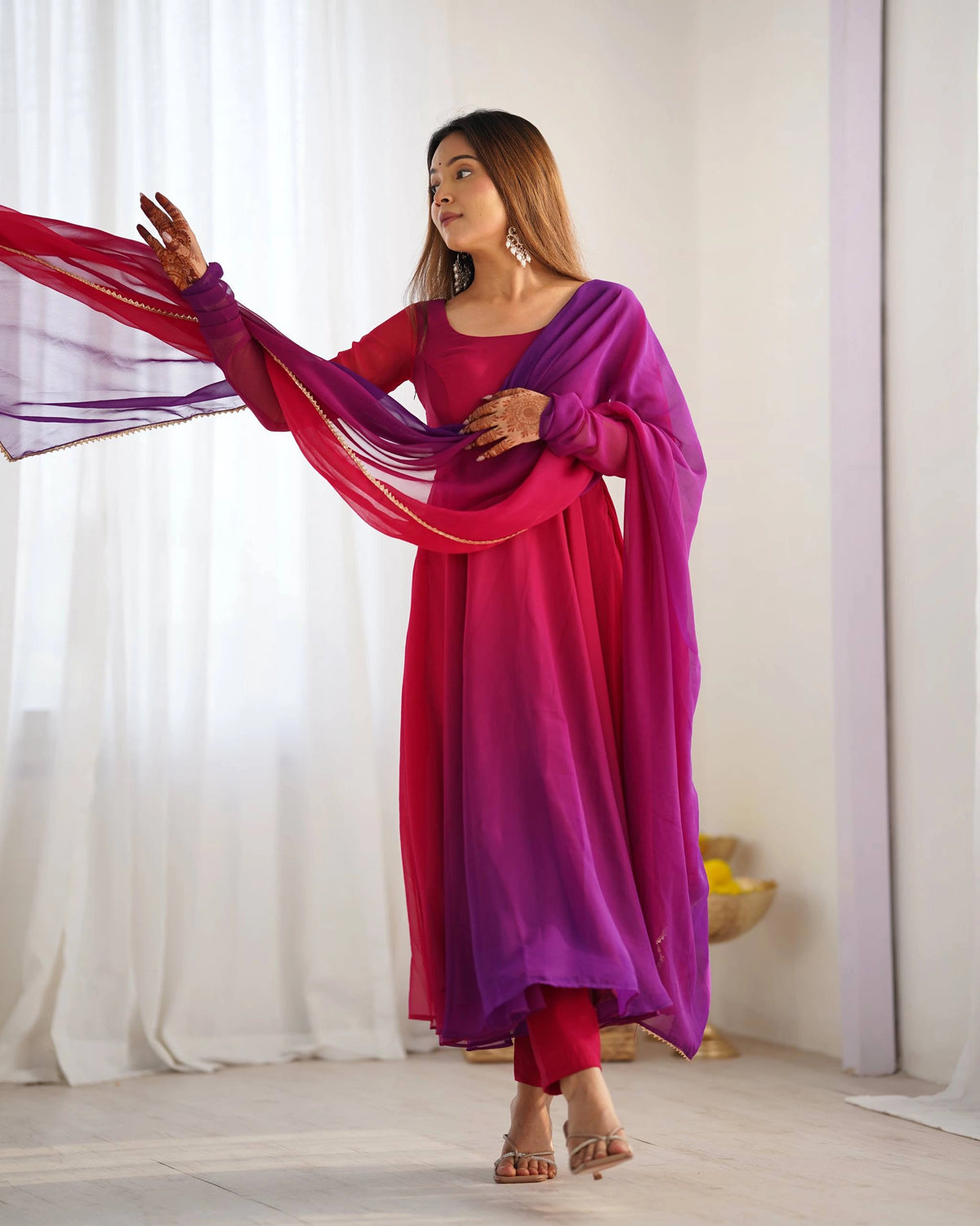 Woman holding a pink and purple dupatta against a white curtain background