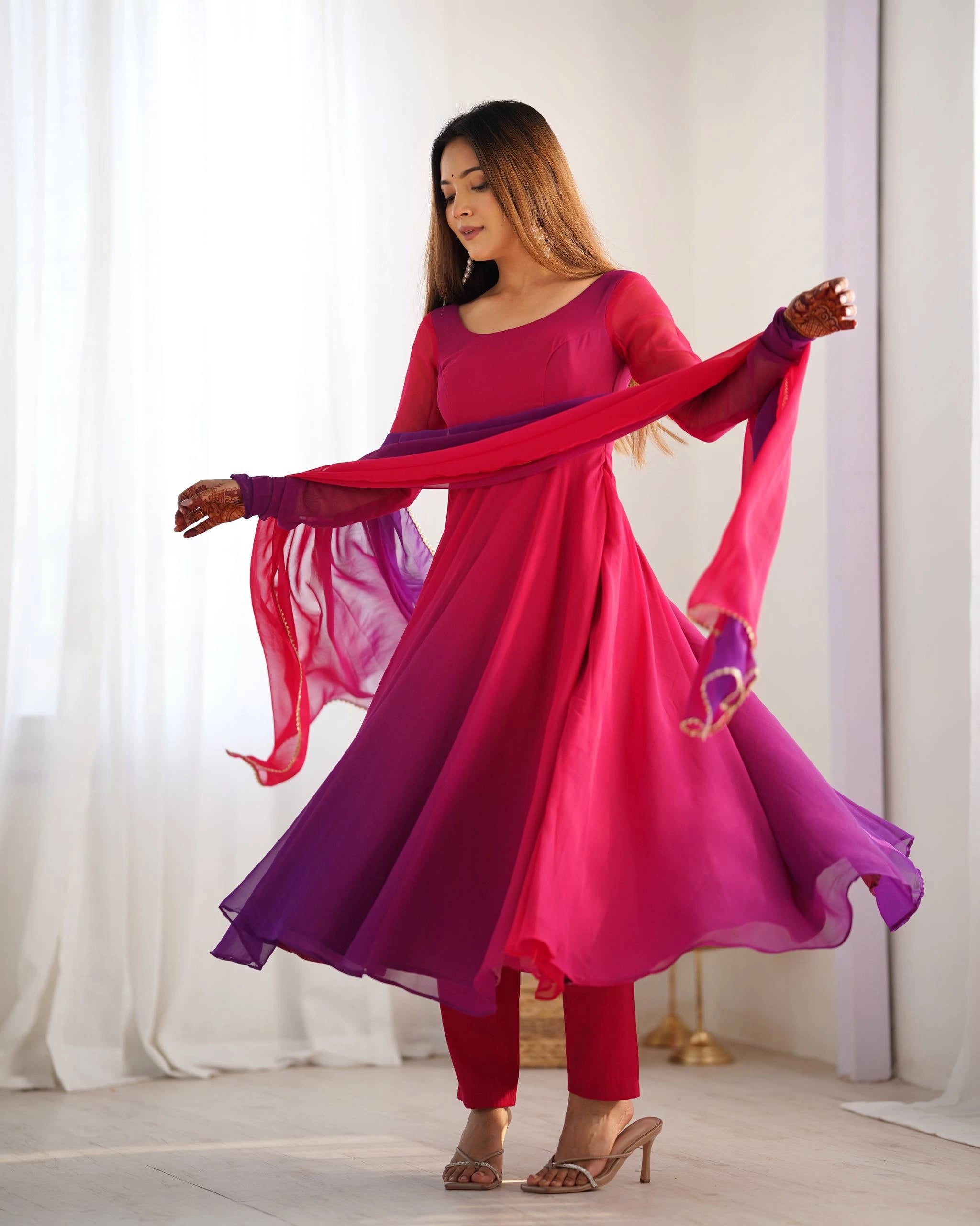 A dynamic full-length shot of a woman in a magenta and purple ethnic suit, slightly twisting and pulling the matching dupatta straight across her body.