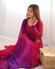 A close-up portrait of a smiling woman wearing a matching magenta and purple ethnic suit, with her hands resting on her chest showcasing detailed henna patterns.