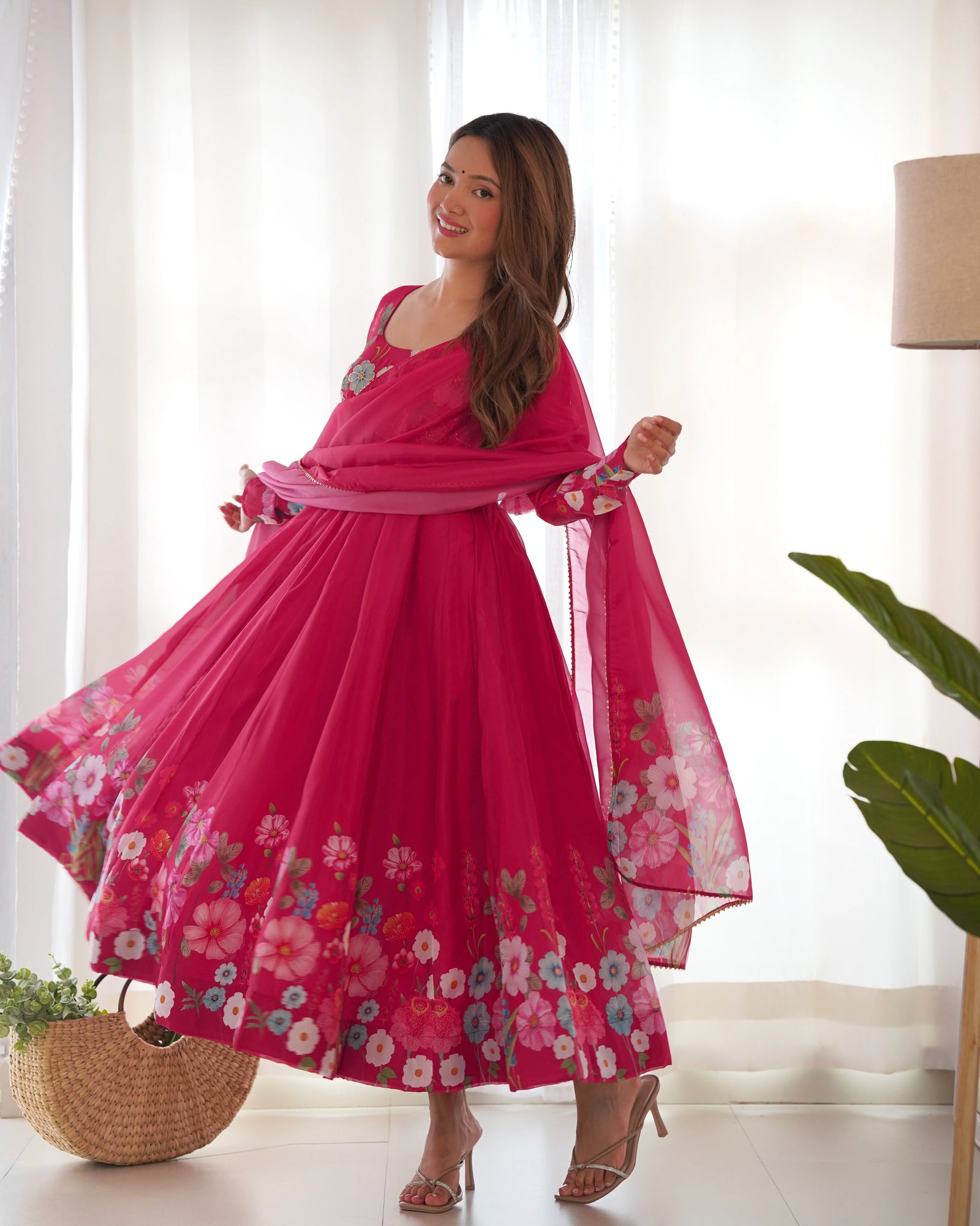 Woman wearing a pink floral dress in a bright room with white curtains.